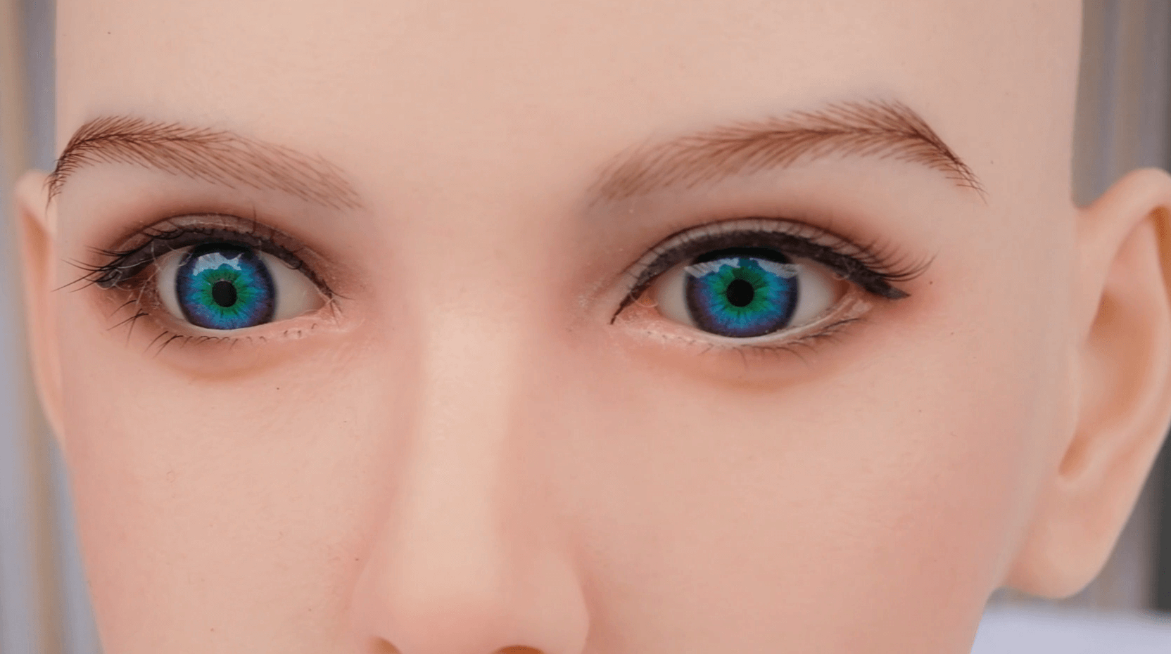Close-up of sex doll makeup showing hand-implanted eyebrows, shaded eyeshadow, defined eyeliner, rooted lashes, and blue-green realistic eyes.